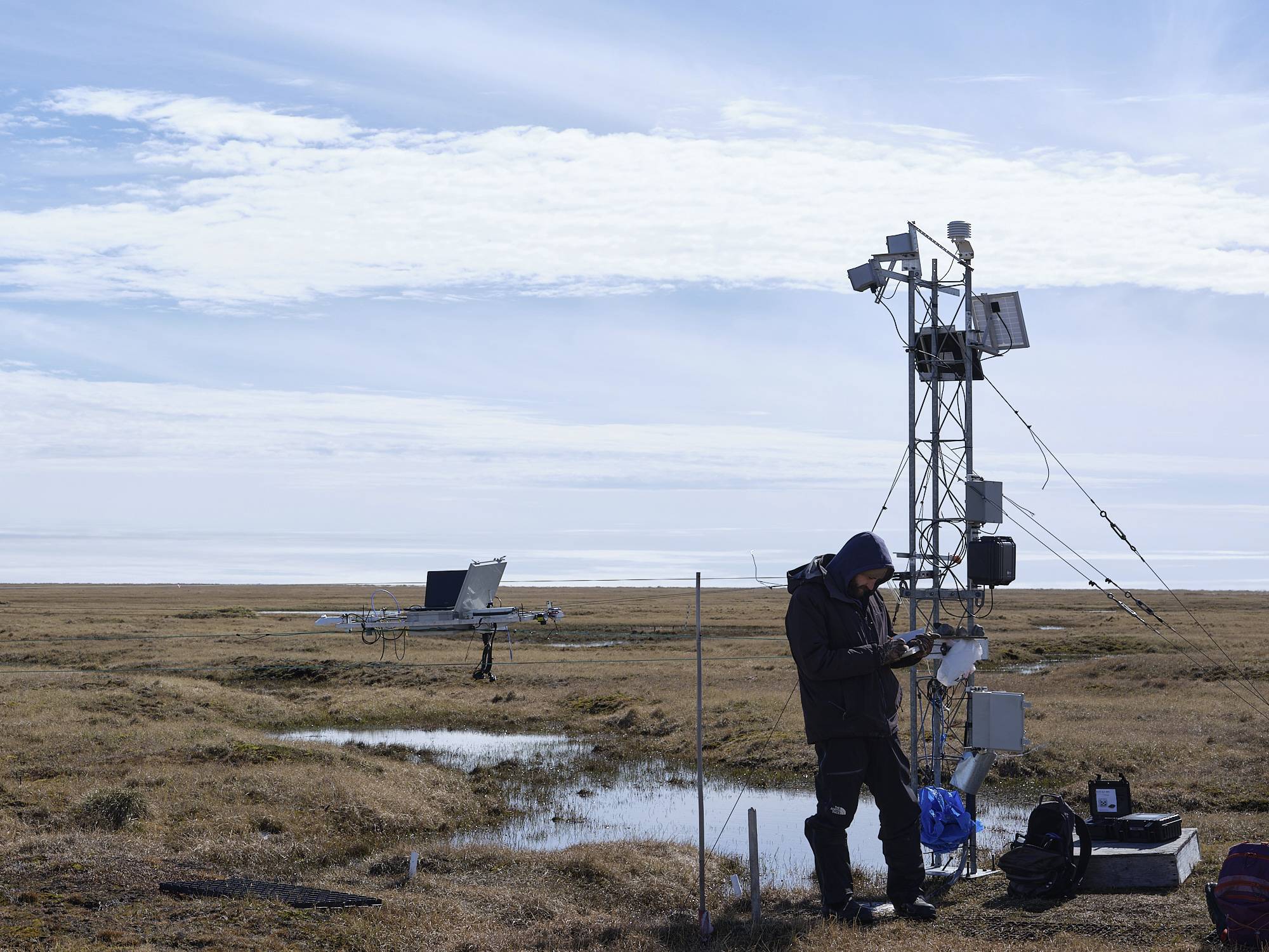 Scott running the tram. A man stands near a tower in a field, recording notes.